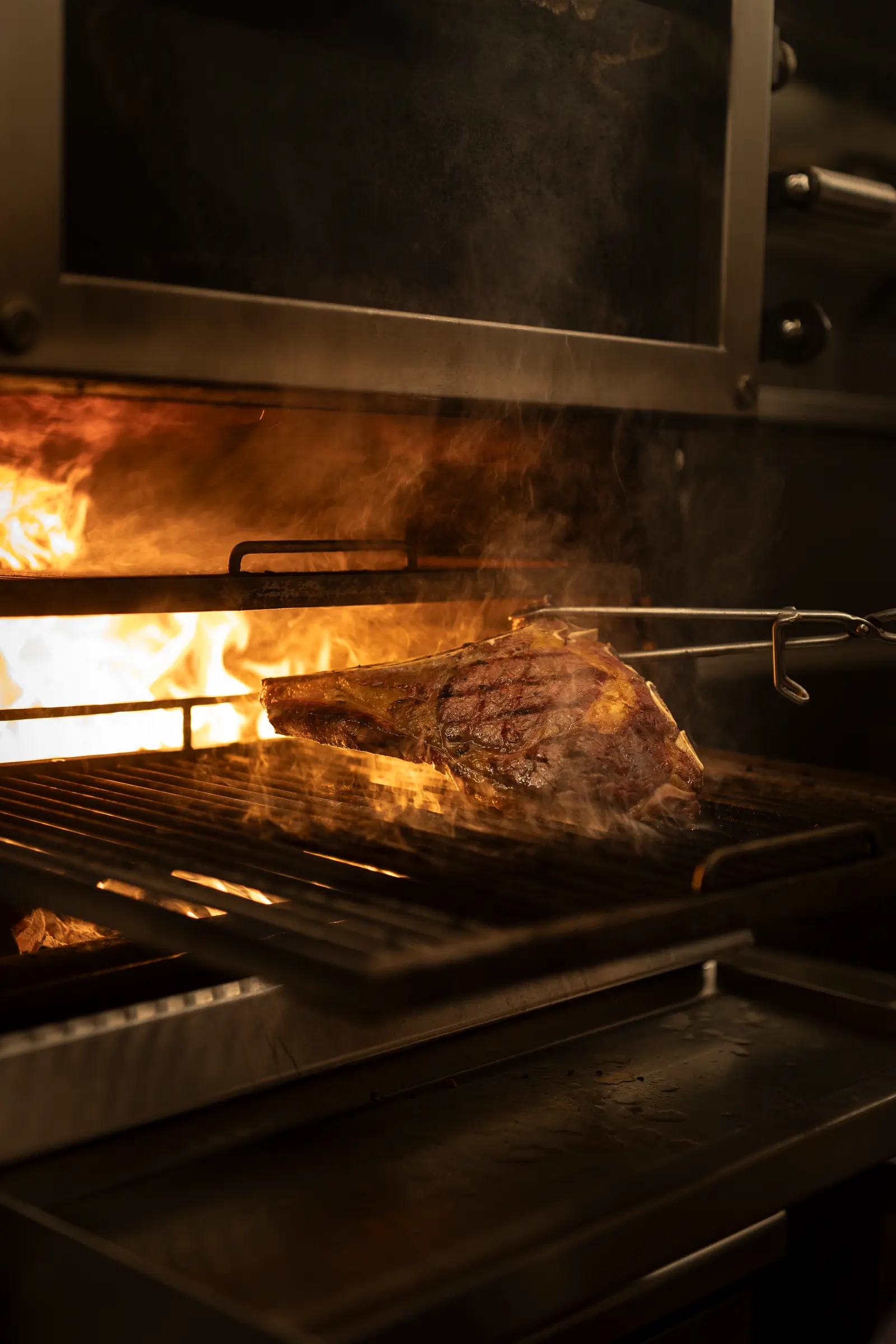 Een steak hangt te roken boven de houtskoolgrill