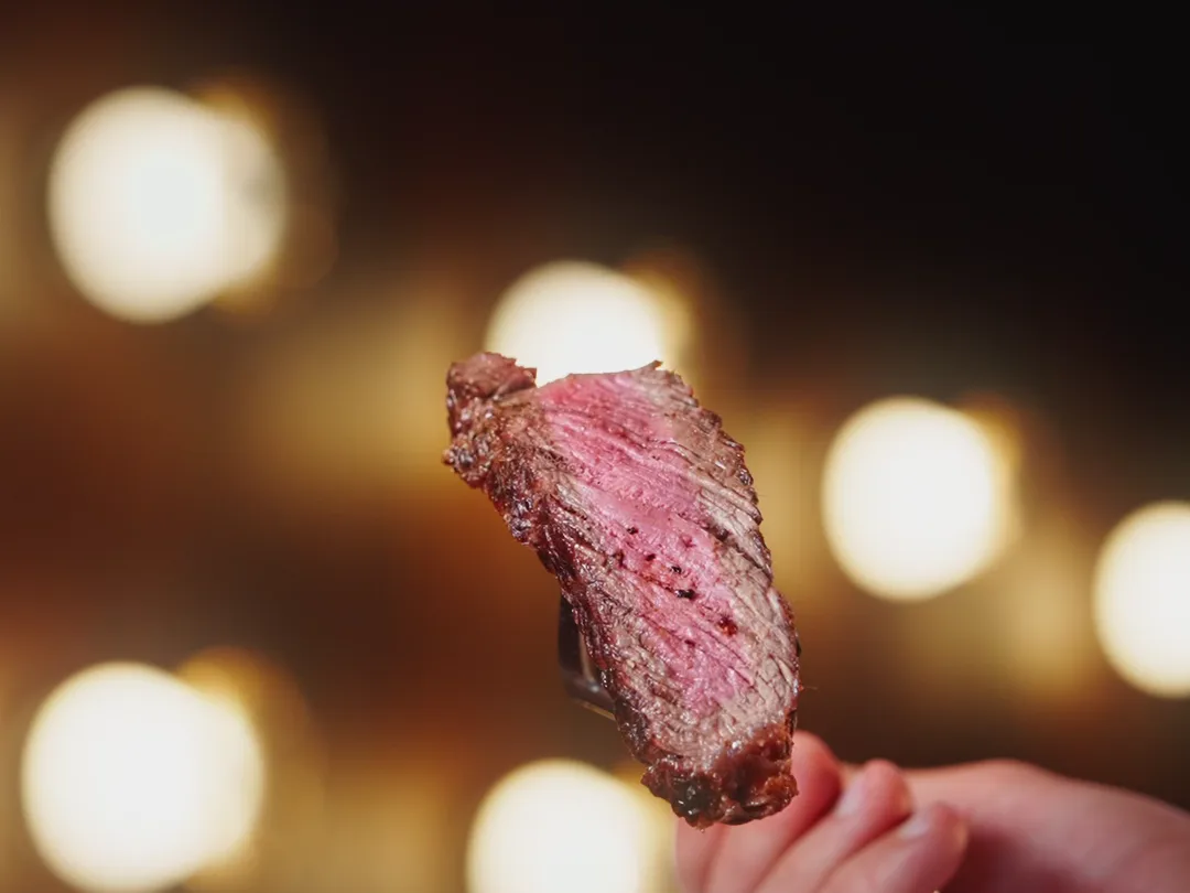 A rosé slice of steak in front of the lights of the dining room